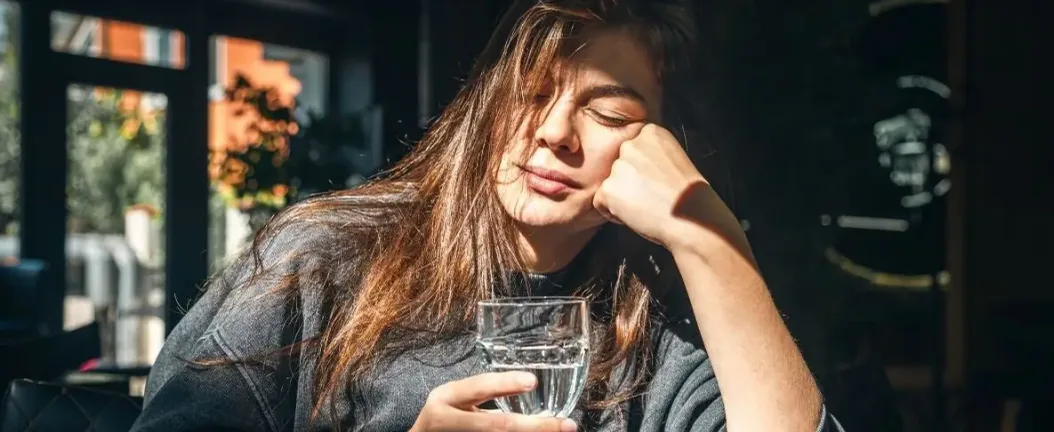 Woman resting her head on her hand while holding a glass of water