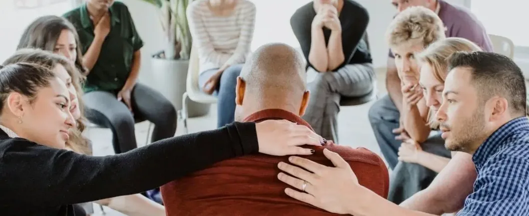 Support group members comforting a man during a group therapy session